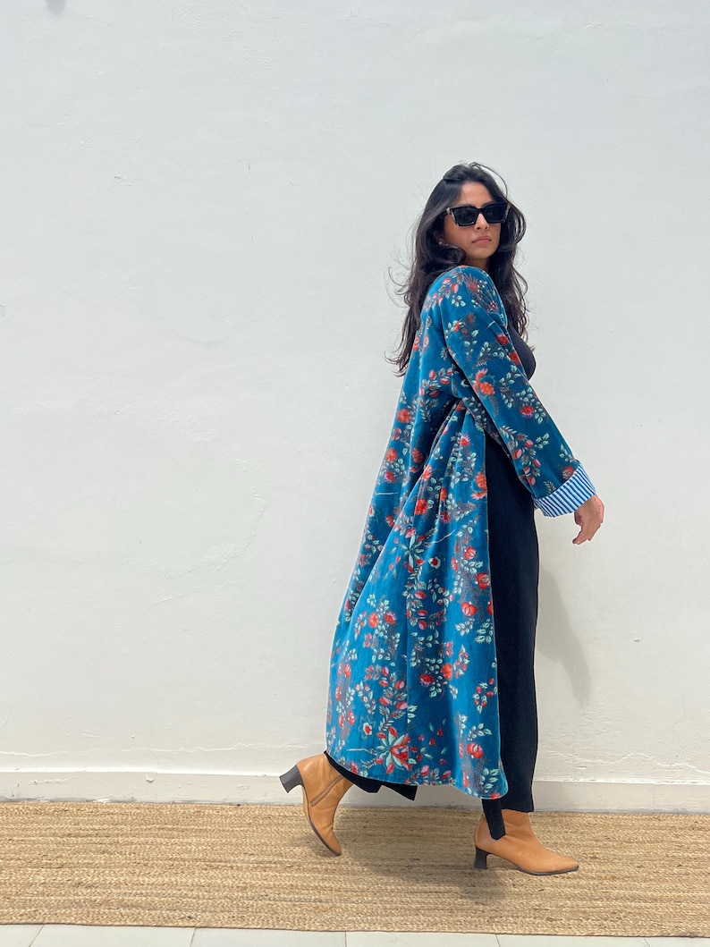 May include: A long, flowing teal floral print robe with red and orange flowers. The robe has a blue and white striped cuff. The person is wearing black pants and brown boots.