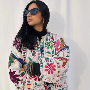May include: A white bomber jacket with colorful floral embroidery. The jacket has a zipper closure and a stand-up collar.