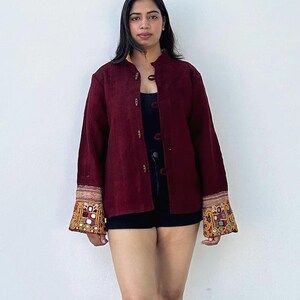 May include: A maroon button-up jacket with embroidered detailing on the cuffs. The jacket has a mandarin collar and is made of a soft, textured fabric.
