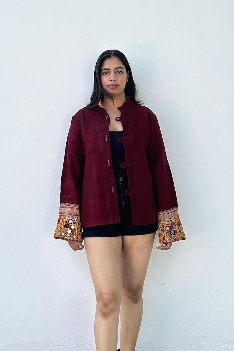 May include: A maroon button-up jacket with embroidered detailing on the cuffs. The jacket has a mandarin collar and is made of a soft, textured fabric.