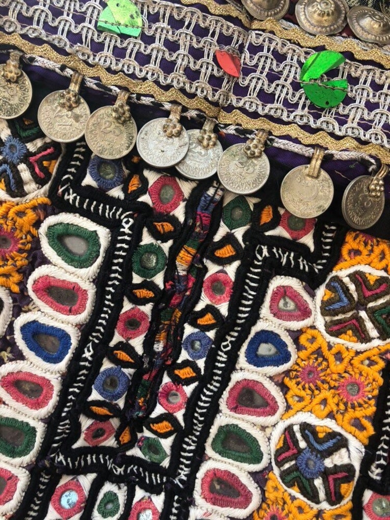 Puede incluir: Primer plano de un textil colorido con intrincados bordados y adornos. El dise&ntilde;o presenta una mezcla de colores vibrantes, incluyendo rojo, amarillo, verde y azul, con acentos de monedas de plata. El textil tiene una apariencia detallada y artesanal.