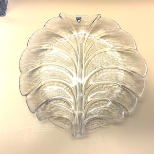 May include: A clear glass serving dish shaped like a leaf. The dish has a textured surface and a raised centre.