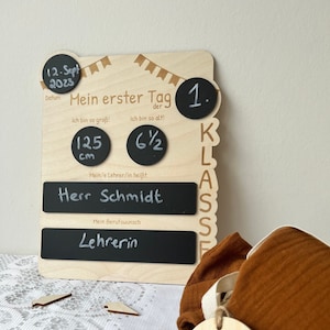 May include: A wooden sign with chalkboard inserts for a first day of school celebration. The sign includes the date "12. Sept 2023", the text "Mein erster Tag der 1. Klasse", and the text "Herr Schmidt". The sign also includes a chalkboard for the child's height, which reads "125 cm" and a chalkboard for the child's age, which reads "6 1/2". The sign also includes a chalkboard for the child's teacher's name and a chalkboard for the child's dream job. The sign is decorated with a banner of flags.