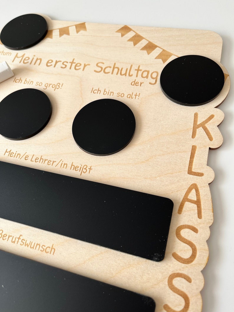 May include: Wooden sign with black chalkboard circles and a rectangular chalkboard. The sign says "Mein erster Schultag" (My first day of school) and "der" (the) and "Ich bin so gro&szlig;!" (I am so big!) and "Ich bin so alt!" (I am so old!) and "Mein/e Lehrer/in hei&szlig;t" (My teacher's name is) and "Berufswunsch" (Career wish). The sign also has the word "KLASS" (Class) written on it.