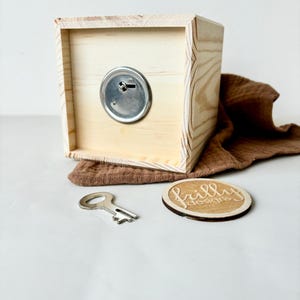 May include: A wooden box with a keyhole and a metal key. The box is sitting on a white surface with a brown fabric and a wooden circle with the text "frilly designs" on it.