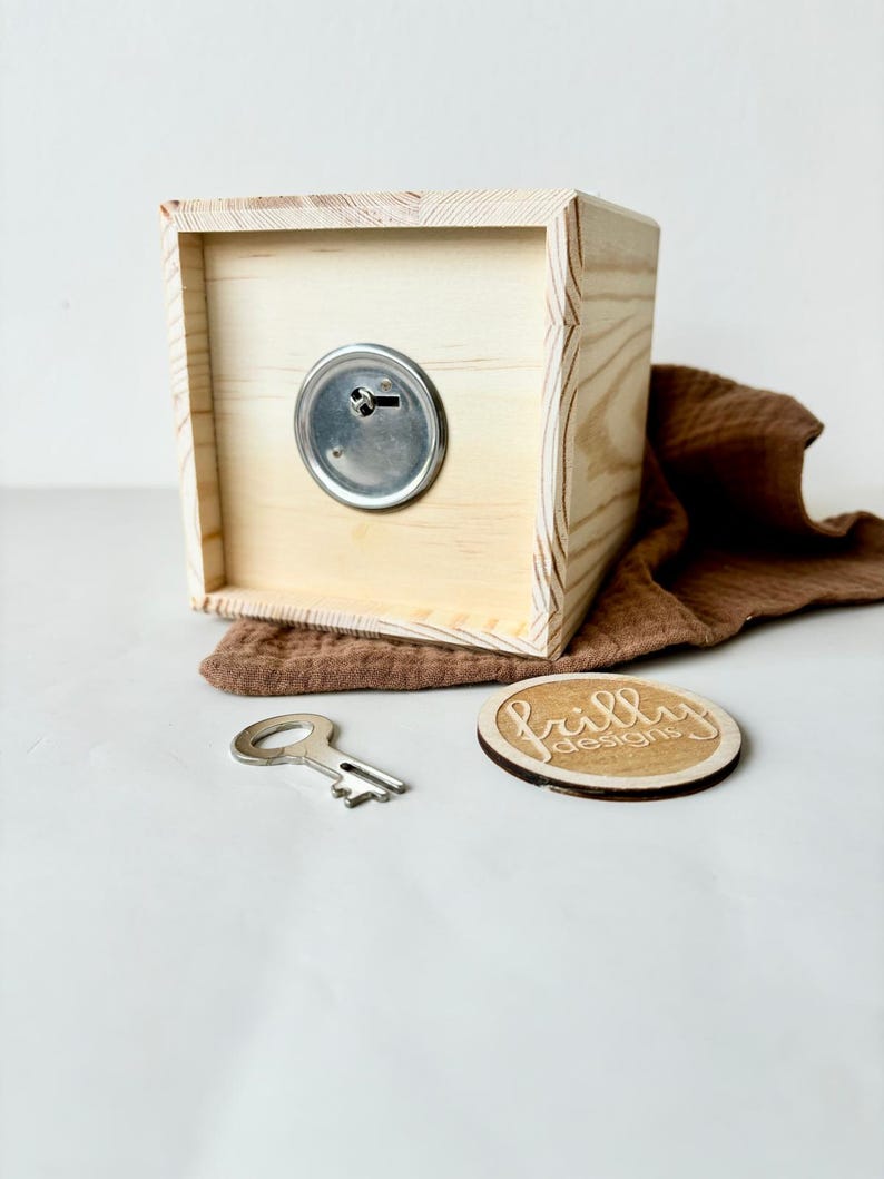 May include: A wooden box with a keyhole and a metal key. The box is sitting on a white surface with a brown fabric and a wooden circle with the text "frilly designs" on it.