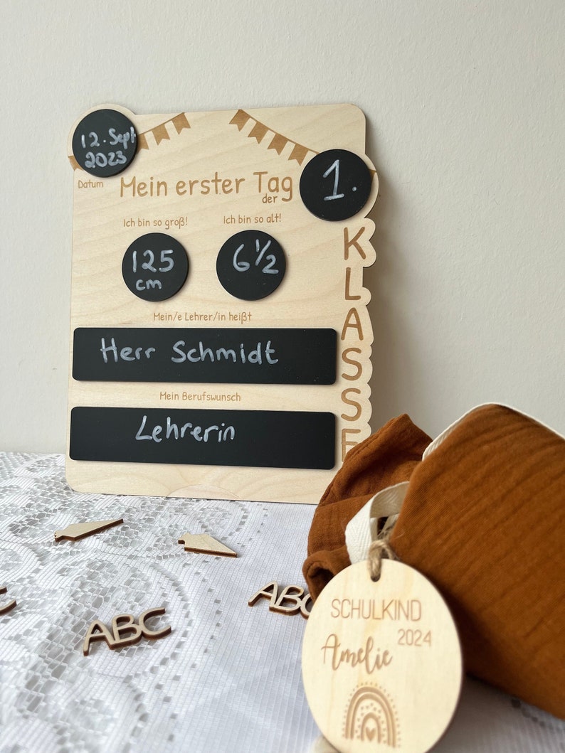 May include: A wooden sign with chalkboard inserts for a first day of school celebration. The sign includes the date "12. Sept 2023", the text "Mein erster Tag der 1. Klasse", and the text "Herr Schmidt". The sign also includes a chalkboard for the child's height, which reads "125 cm" and a chalkboard for the child's age, which reads "6 1/2". The sign also includes a chalkboard for the child's teacher's name and a chalkboard for the child's dream job. The sign is decorated with a banner of flags.
