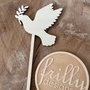 May include: Wooden dove with an olive branch in its beak, on a stick, with a round wooden sign that says "frilly designs".