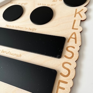 May include: Wooden sign with the text "Mein erster Schultag" (My first day of school) and "KLASSE" (Class). The sign has several black chalkboard areas for writing, including spaces for "Ich bin so gro&szlig;!" (I am so big!), "Ich bin so alt!" (I am so old!), "Mein/e Lehrer/in hei&szlig;t" (My teacher's name is), and "Berufswunsch" (Career wish).