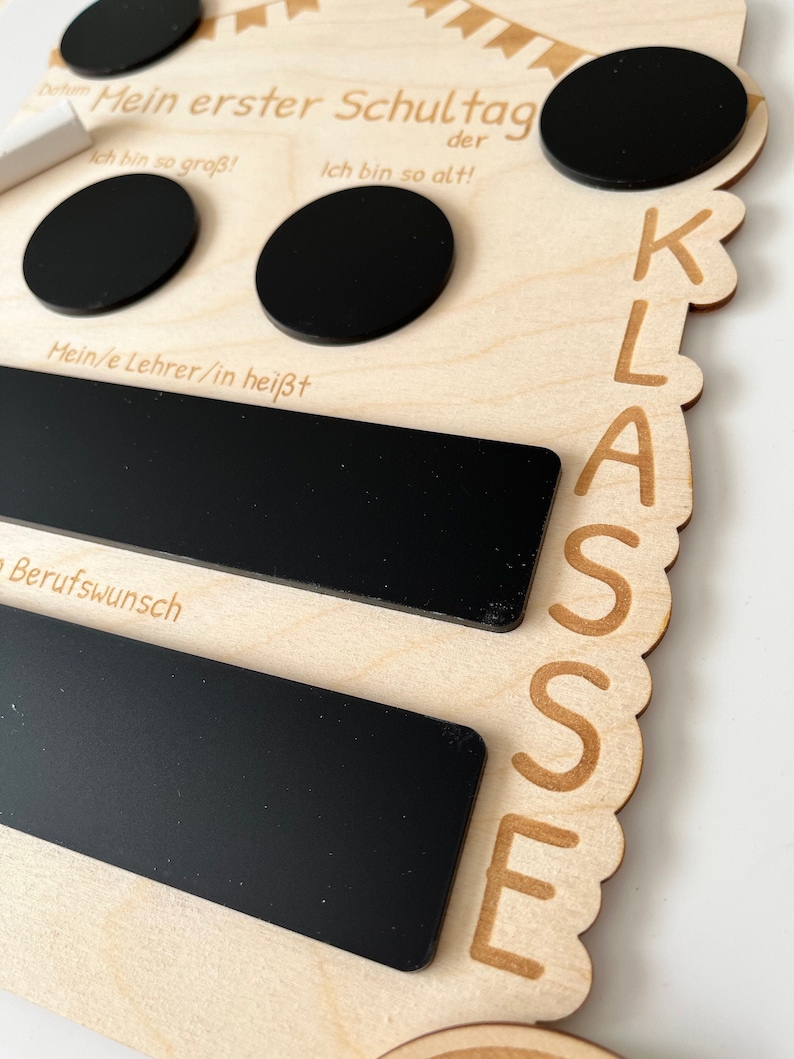 May include: Wooden sign with the text "Mein erster Schultag" (My first day of school) and "KLASSE" (Class). The sign has several black chalkboard areas for writing, including spaces for "Ich bin so gro&szlig;!" (I am so big!), "Ich bin so alt!" (I am so old!), "Mein/e Lehrer/in hei&szlig;t" (My teacher's name is), and "Berufswunsch" (Career wish).