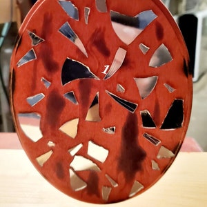 May include: A round, red wooden ornament with a string for hanging. The ornament is decorated with a mosaic of small, broken mirror pieces.