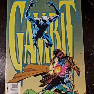May include: A comic book cover for "Gambit" by Marvel Comics. The cover features a dynamic illustration of Gambit in action, with a figure in blue leaping above him. The comic is a direct edition, with the price $2.00 US.
