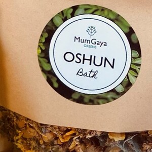 May include: A brown paper bag with a white circular sticker. The sticker features a green plant illustration and the text "MumGaya Greens" and "OSHUN Bath".
