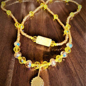 May include: A yellow beaded necklace with a cork bead and a gold sunflower charm.