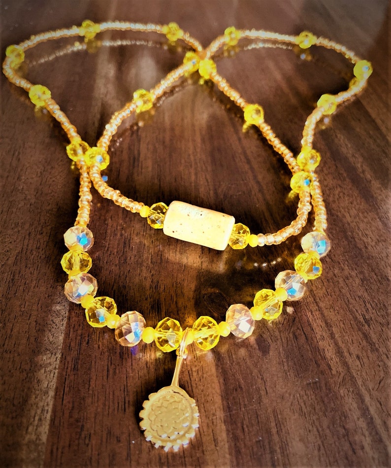 May include: A yellow beaded necklace with a cork bead and a gold sunflower charm.