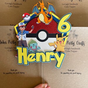 Könnte beinhalten: Ein handgemachter Tortendekor im Pokémon-Thema. Der Dekor enthält einen roten und orangen Glurak, einen blauen und weißen Pokéball, einen grünen Bisasam, einen gelben Pikachu, eine blaue und gelbe Nummer 6 und den Namen Henry in gelben Buchstaben. Der Dekor befindet sich auf einem braunen Hintergrund mit dem Text "Inka Party Crafts" und "Lovingly handmade Cake Topper".