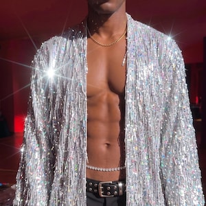 May include: A silver sequined open-front kimono-style jacket with long sleeves and a fringe-like texture. The garment is covered in reflective, shimmering sequins that catch the light, creating a metallic, high-shine appearance throughout.