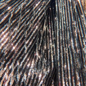 May include: A black fabric garment featuring vertical rows of shimmering silver sequins. The material is adorned with long, dangling fringe strands covered in reflective sequins that catch the light, creating a dense and textured appearance.