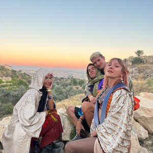 May include: A group of people wearing sequined hooded cloaks, patterned robes, fishnet stockings, and leather boots. The garments feature metallic gold and silver sequins, intricate embroidery, and layered fabrics in shades of red, blue, and tan.
