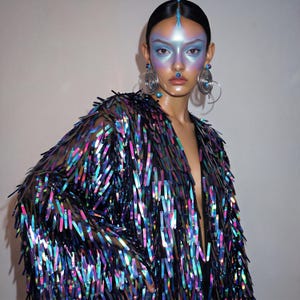May include: A long-sleeved jacket covered in iridescent, rectangular, metallic sequins that shift between shades of blue, purple, and green. The garment features a deep V-neckline and a black base fabric, creating a high-contrast, reflective surface.
