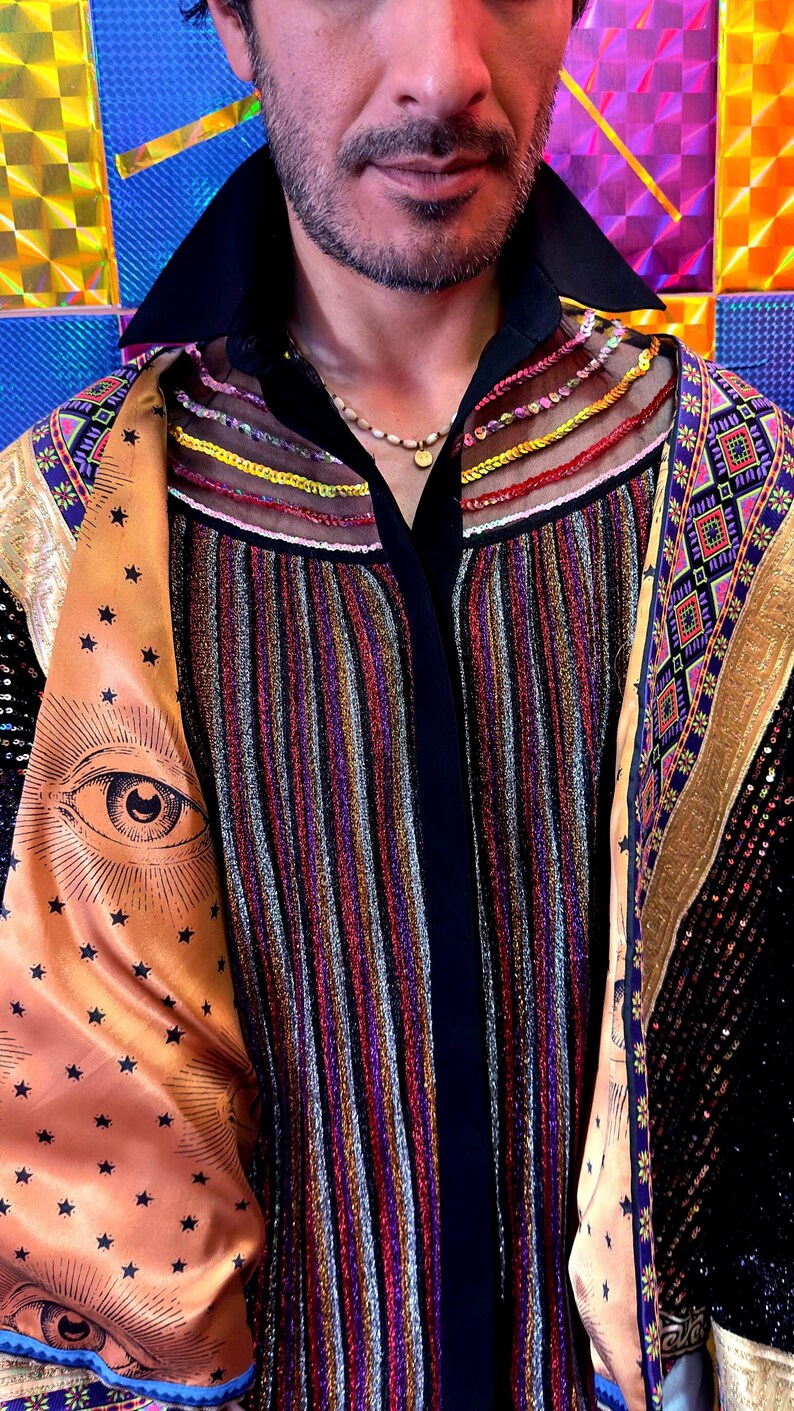 May include: A multi-colored striped shirt featuring a black collar and sheer mesh panels at the neckline with horizontal embroidery. The garment includes gold-toned satin lapels printed with black star patterns and eye illustrations, layered over a black base.