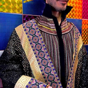 May include: A long-sleeved jacket featuring black sequined sleeves, a central panel with vertical multicolored stripes, and wide decorative borders with gold Greek key patterns and intricate geometric squares in purple, pink, and teal.
