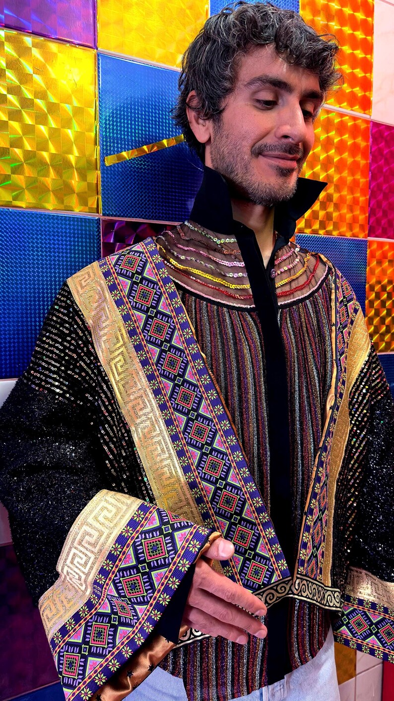 May include: A long-sleeved jacket featuring black sequined sleeves, a central panel with vertical multicolored stripes, and wide decorative borders with gold Greek key patterns and intricate geometric squares in purple, pink, and teal.