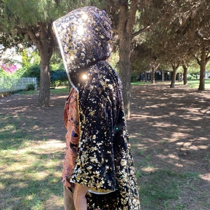 Può includere: Un mantello con cappuccio nero e dorato con paillettes, con un design lungo e fluido. Il mantello è realizzato in un tessuto morbido e lussuoso e presenta una finitura scintillante e iridescente.