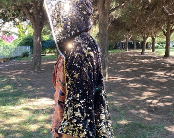 May include: A black and gold sequined hooded cape with a long, flowing design. The cape is made of a soft, luxurious fabric and features a shimmering, iridescent finish.