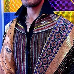 May include: A black button-down shirt featuring a vertical metallic striped panel, a sheer yoke with horizontal beaded rows, and a wide satin shoulder panel printed with a large eye and star motif, accented by a decorative blue and gold geometric trim.