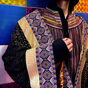 May include: A long-sleeved jacket featuring a black sequined base, a high black collar, and a metallic gold trim with a Greek key pattern. The garment includes panels of multicolored geometric embroidery, sheer mesh sections, and vertical metallic stripes.