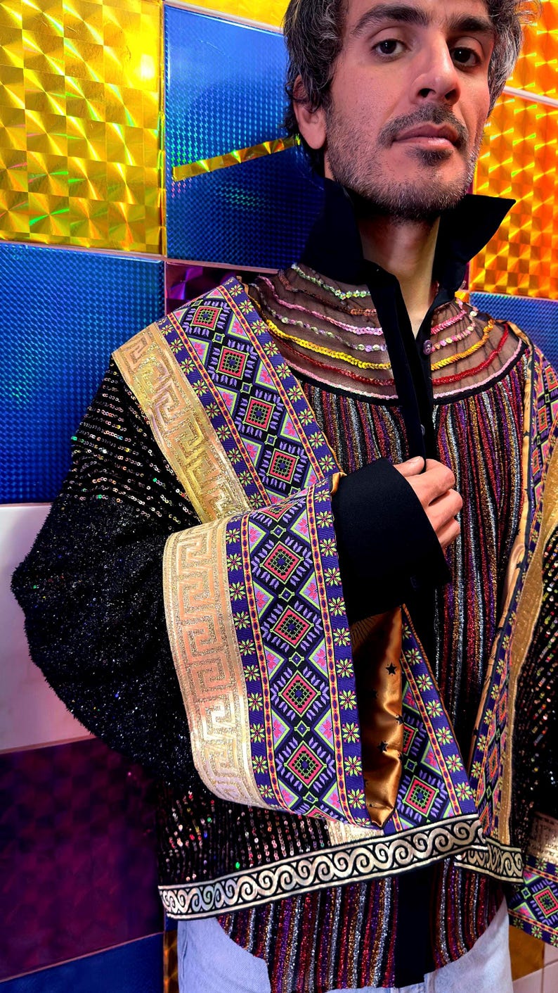 May include: A long-sleeved jacket featuring a black sequined base, a high black collar, and a metallic gold trim with a Greek key pattern. The garment includes panels of multicolored geometric embroidery, sheer mesh sections, and vertical metallic stripes.