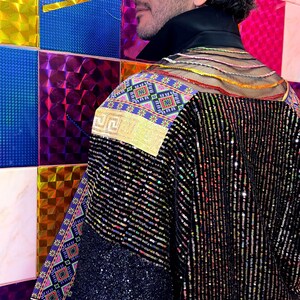 May include: A black jacket featuring vertical sequin stripes, a high black collar, and a sheer upper back panel with horizontal colorful threads. The shoulders and sleeves are accented with panels of vibrant, multi-colored geometric patterns.