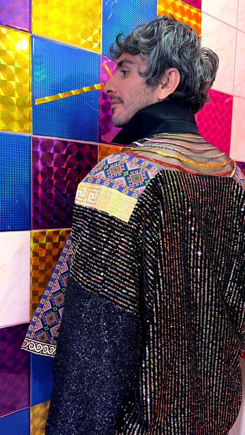 May include: A black jacket featuring vertical sequin stripes, a high black collar, and a sheer upper back panel with horizontal colorful threads. The shoulders and sleeves are accented with panels of vibrant, multi-colored geometric patterns.
