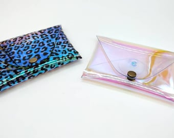 May include: Two small, rectangular pouches. One features a blue and black leopard print, and the other is transparent with a pink and yellow iridescent sheen. Both have a snap closure.