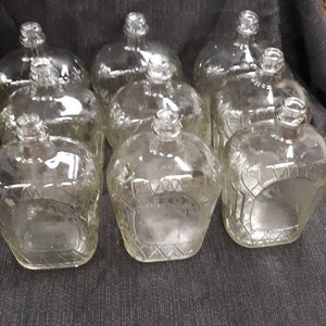 May include: Eight clear glass bottles with a textured surface. The bottles are arranged in two rows of four.