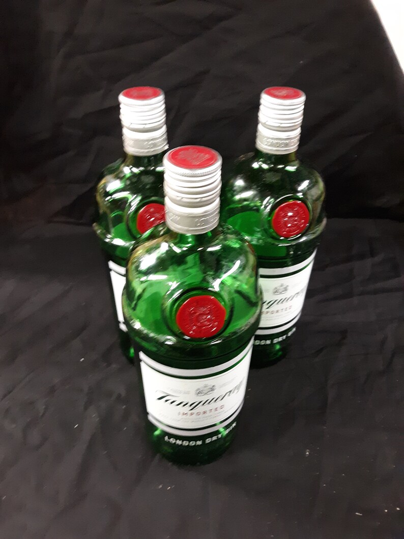 May include: Three green glass bottles of Tanqueray London Dry Gin with red and white labels. The bottles are on a black surface.
