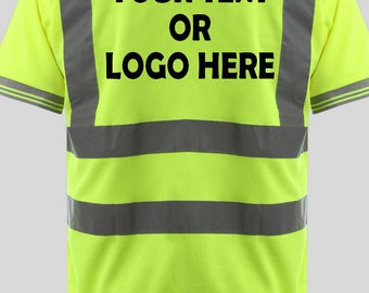 Può includere: Una polo di colore giallo brillante con strisce riflettenti argentate. La parte posteriore della polo ha un testo nero che dice "YOUR TEXT OR LOGO HERE".