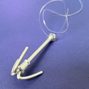 May include: A silver-colored hook with a clear plastic string attached. The hook has a triple hook design and is designed for hanging items.