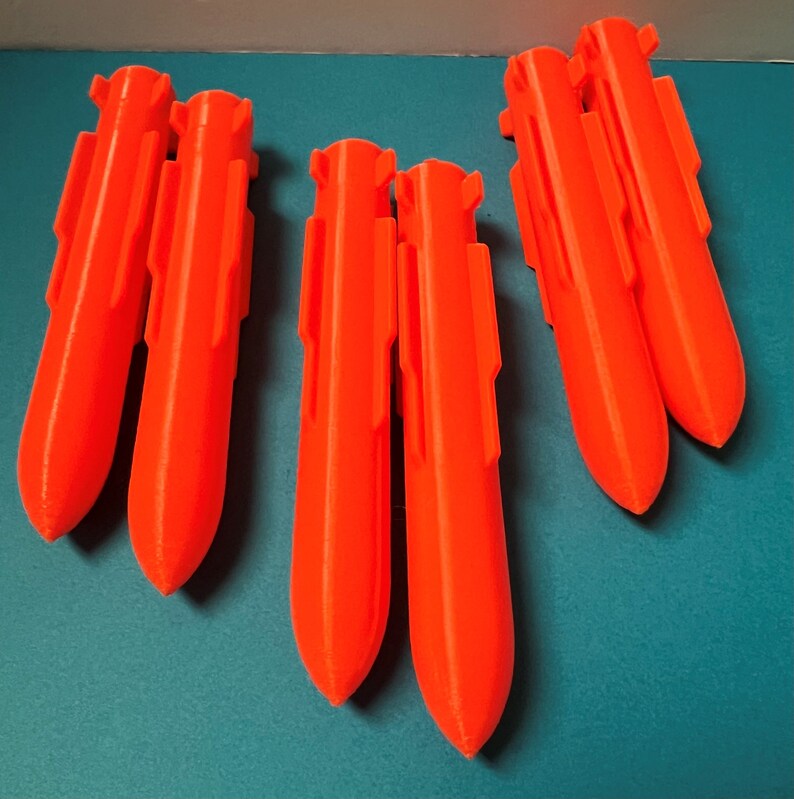 May include: Five bright orange plastic toy rockets, each with a pointed nose and fins. The rockets are arranged in two groups of two and one single rocket.