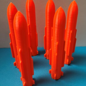 May include: Six bright orange plastic rockets, standing upright on a blue surface. The rockets have a pointed top and a slightly flared base.