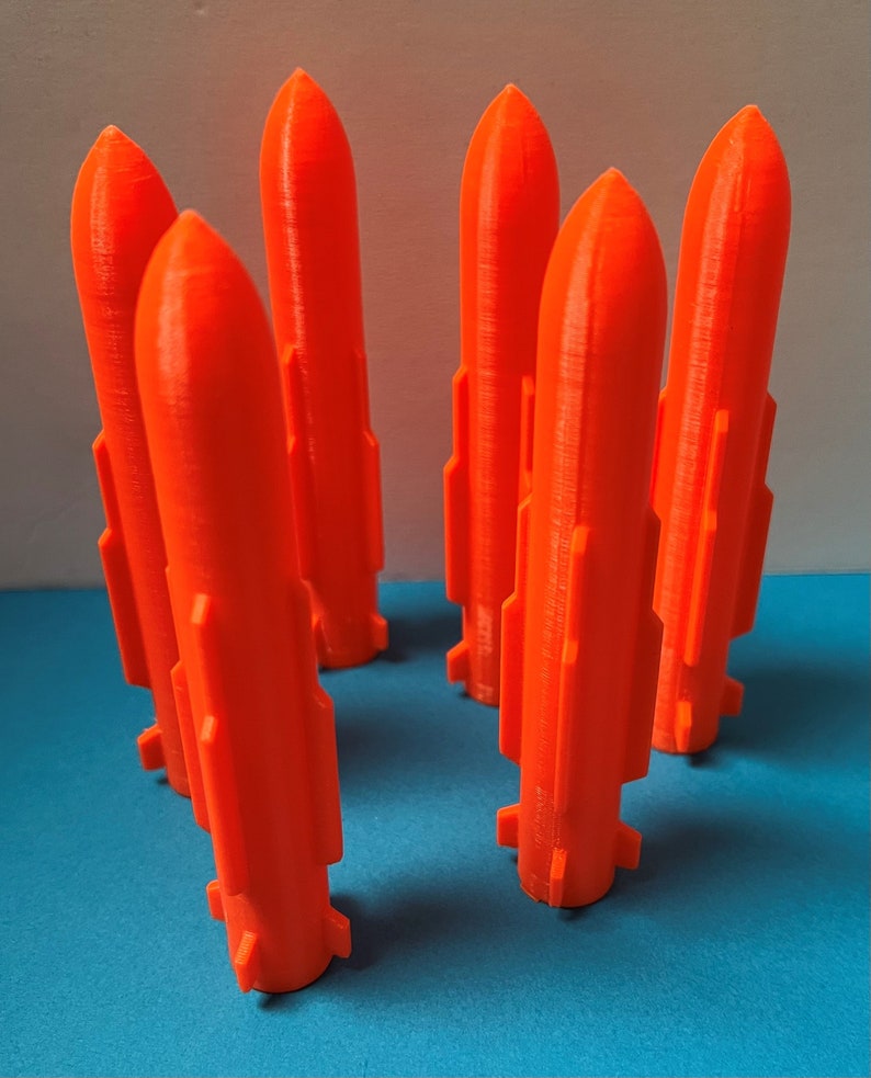 May include: Six bright orange plastic rockets, standing upright on a blue surface. The rockets have a pointed top and a slightly flared base.