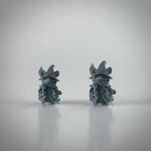 May include: Two gray figurines of mice dressed as wizards. Each mouse wears a pointed hat, a cloak, and carries a staff. The figurines are detailed with small pouches and other accessories, suggesting a fantasy theme.