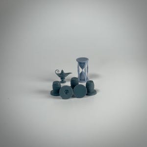 May include: A collection of small, gray decorative objects. The items include an hourglass, a genie lamp, bottle stoppers, and barrel-shaped items. The bottle stoppers have a skull design. The objects are arranged on a white surface.