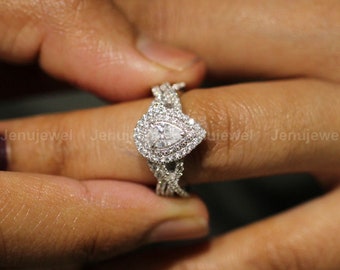 Puede incluir: Un anillo de compromiso de diamante de forma pera con un engaste halo. El anillo está engastado en una banda de oro blanco con un diseño trenzado.