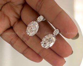 May include: A pair of silver dangle earrings with large oval-shaped clear cubic zirconia stones. The earrings have a smaller clear cubic zirconia stone above the larger stone.