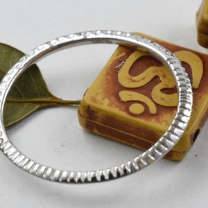 May include: A silver ring with a textured design. The ring has a series of small, evenly spaced indentations along the outer edge. The ring is circular and appears to be made of metal. The ring is a jewelry item.