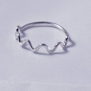 May include: A silver ring with a wavy design. The ring has a continuous, undulating pattern that goes around the finger. The ring is made of a shiny, reflective metal, and is set against a white background.