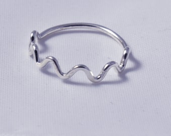 May include: A silver ring with a wavy design. The ring features a continuous, undulating pattern that wraps around the finger. The ring is made of a shiny, reflective metal, and is set against a white background.