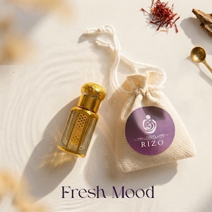May include: A small, clear glass perfume bottle with gold accents and a decorative cap sits next to a small drawstring bag with a purple label. The bag has the word "RIZO" printed on it. The words "Fresh Mood" are at the bottom.